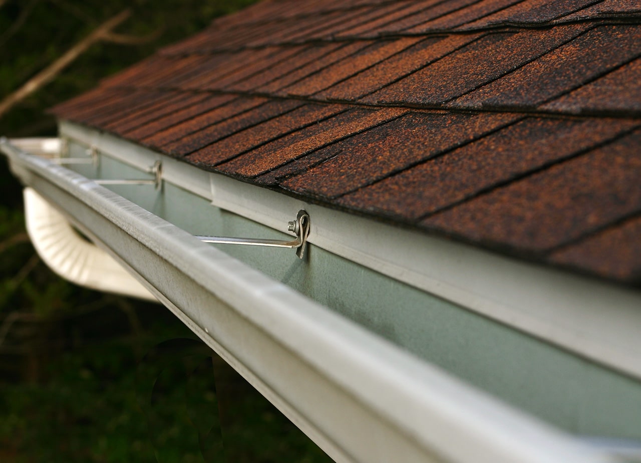 A photo of a roof with a gutter drain installed, advertising Roofing For Troops' gutter cleaning services
