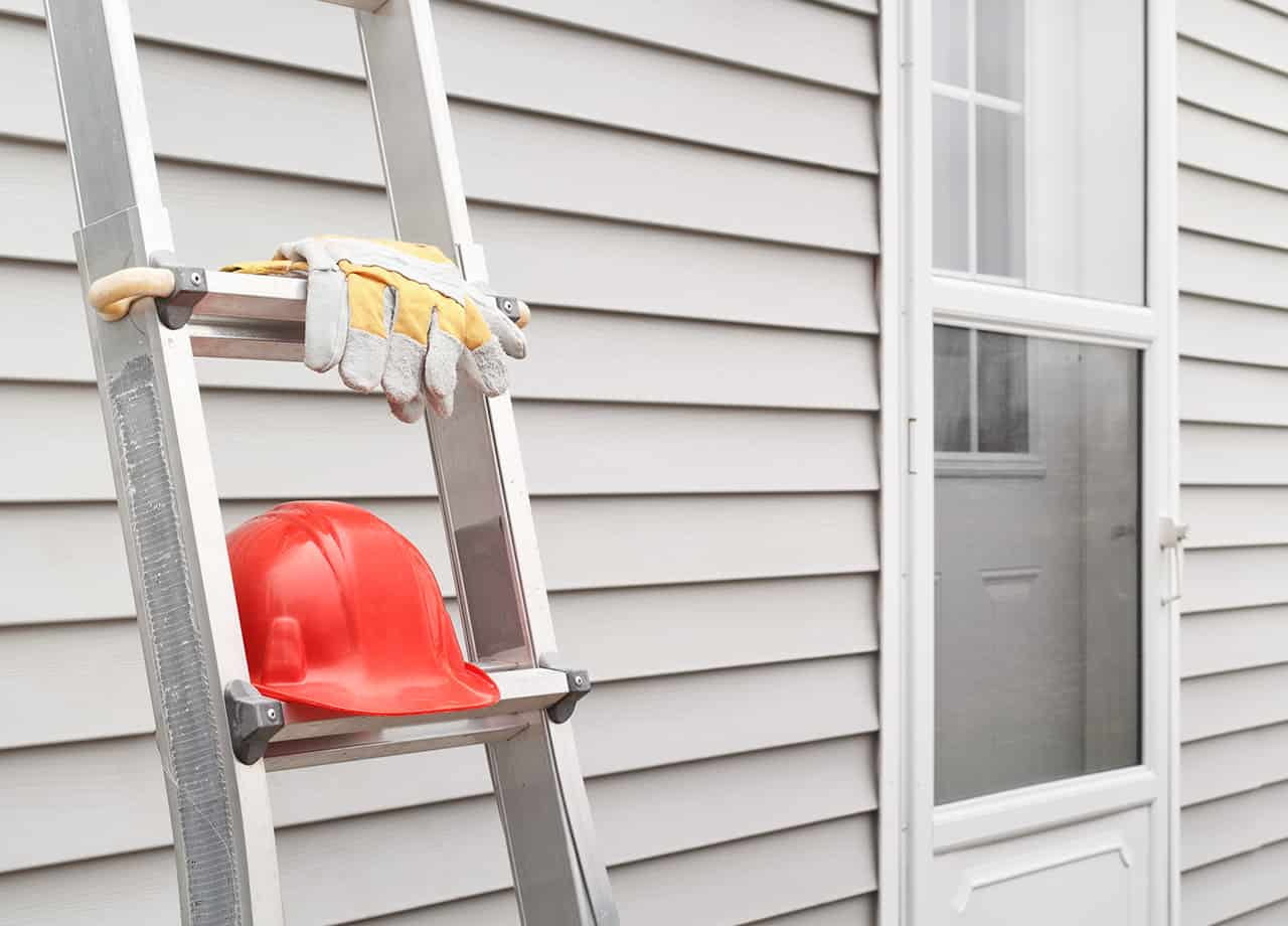 Image of a ladder leaning against the siding on a home with a hard hat and gloves. Roofing For Troops offers professional siding repairs in Milford OH & Cincinnati OH.